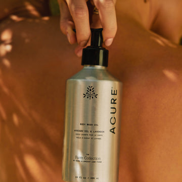 Acure body wash bottle being held against a brown background